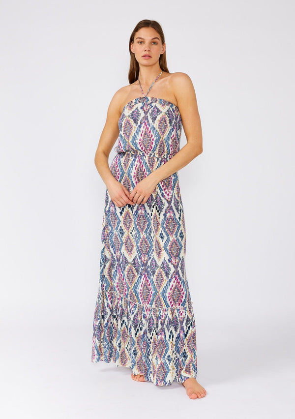 [Color: Natural/Dusty Blue] A front facing image of a brunette model wearing a stunning sleeveless beach maxi dress designed in a blue bohemian print. With a halter neckline and adjustable tie at the back neckline, an elastic waist, and a long flowy skirt with a ruffle trimmed tiered hemline. 
