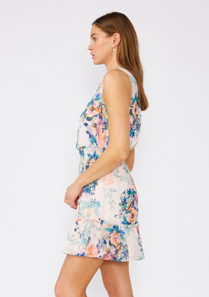 [Color: Peach/Teal] A side facing image of a brunette model wearing a pretty sleeveless mini dress in a pink and teal blue floral print. Designed in chiffon, with a ruffled neckline, a v neck front, a smocked elastic waist, a ruffle trimmed tiered skirt, and a loop button front top. 