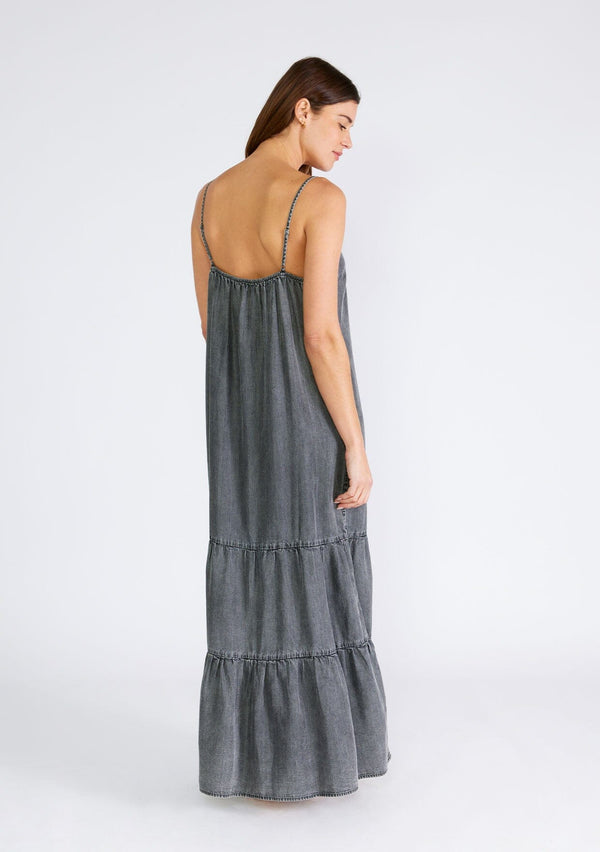 [Color: Ash Grey Wash] A back facing image of a brunette model wearing an ash grey wash sleeveless maxi dress made from Tencel. With adjustable spaghetti straps, a v neckline, and a long flowy tiered silhouette. 
