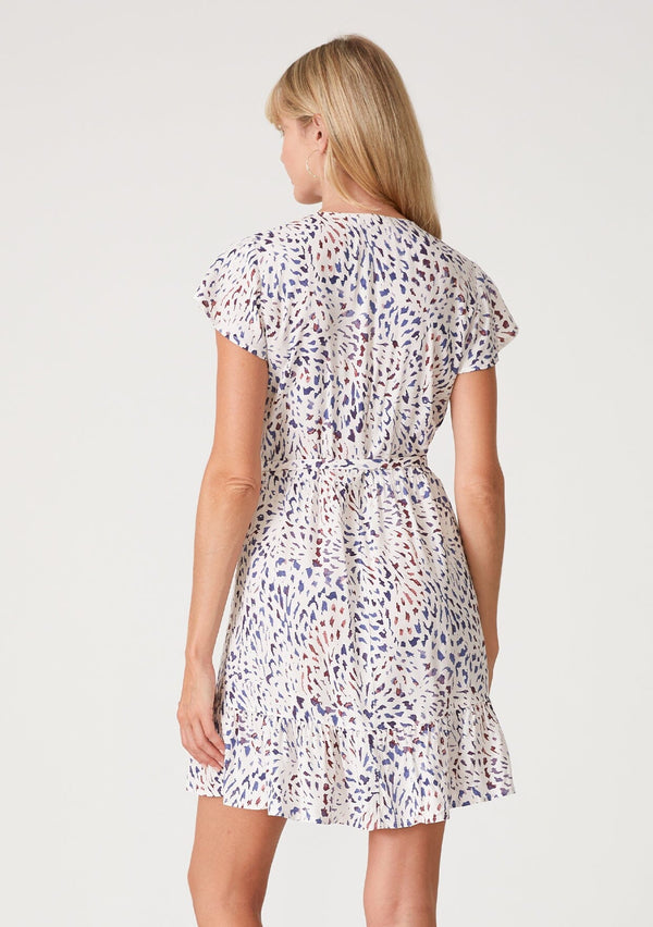 [Color: Natural/Ink] A back facing image of a blonde model wearing a classic fit and flare mini dress in a multi colored abstract print. With short flutter sleeves, a v neckline, a ruffled hemline, and a side tie closure at the waist. 