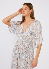 [Color: Cream/Dusty Blue] A close up front facing image of a brunette model wearing a flowy bohemian beach dress in a cream and blue abstract print. With flowy half length sleeves, a v neckline in the front and back, a smocked elastic waist, side slits, and an open back with tie detail. 
