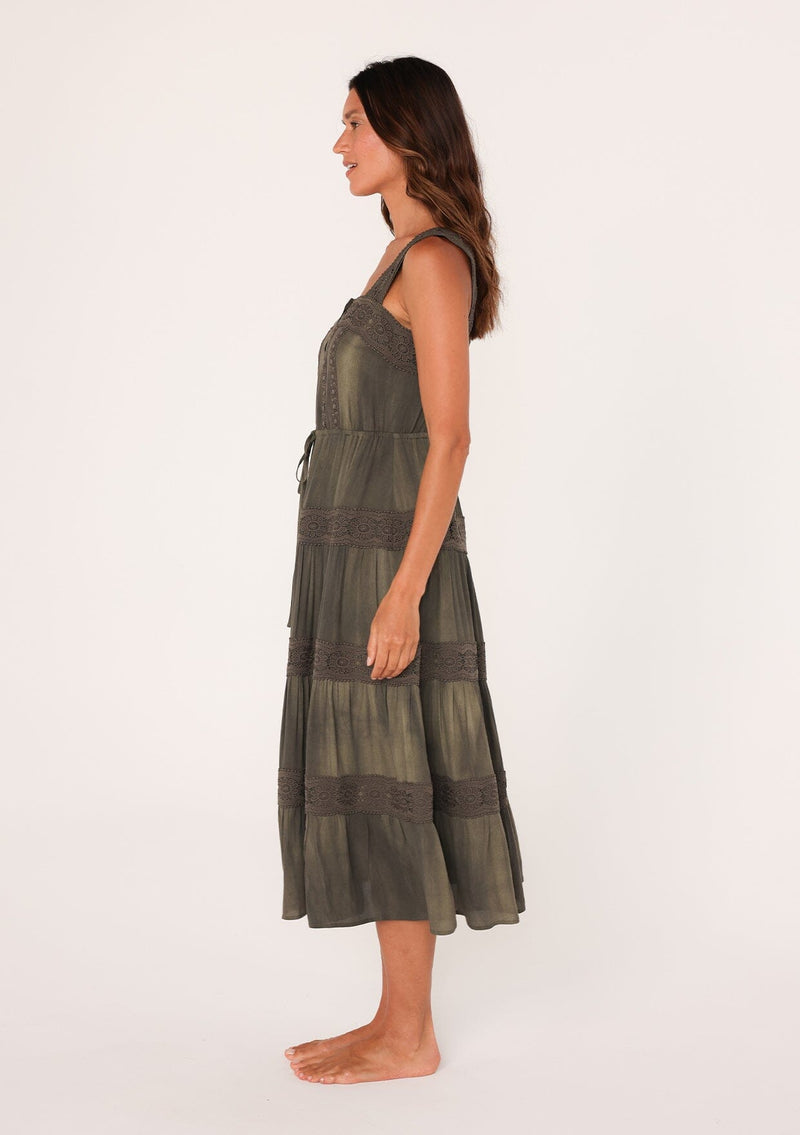 [Color: Olive] A side facing image of a brunette model wearing an olive green bohemian mid length dress. With a square neckline, a tiered flowy skirt, adjustable tank top straps, a button front top, a drawstring tie waist, and lace trim throughout.