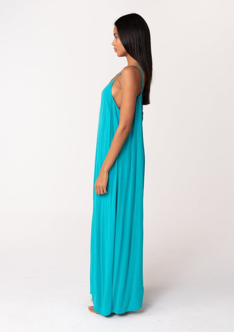 [Color: Turquoise] A side facing image of a brunette model wearing a turquoise blue summer bohemian maxi tank dress. With adjustable spaghetti straps, a v neckline, a flowy fit, and a soutache braided detail at the back. 