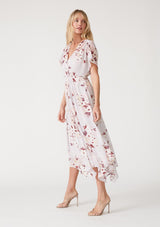 [Color: Dusty Blush/Wine] A side facing image of a blonde model wearing a bohemian maxi dress designed in a pink floral print and crafted from textured chiffon. With short dolman sleeves, a surplice v neckline, an open back with tie closure, and a flowy asymmetric hemline skirt. 