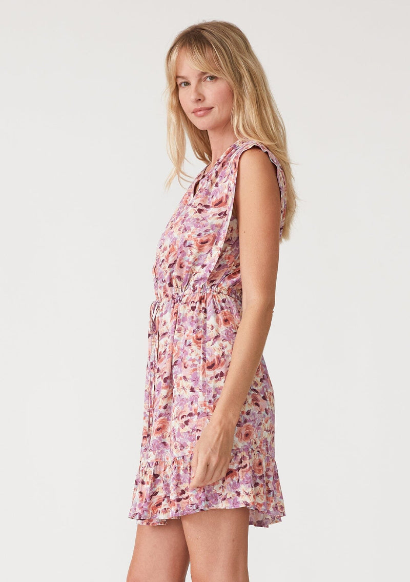 [Color: Dusty Purple/Taupe] A side facing image of a blonde model wearing a pink and purple floral print sleeveless mini dress. With a round neckline, a self covered button front, a tiered mini skirt, and a drawstring waist with ties. 