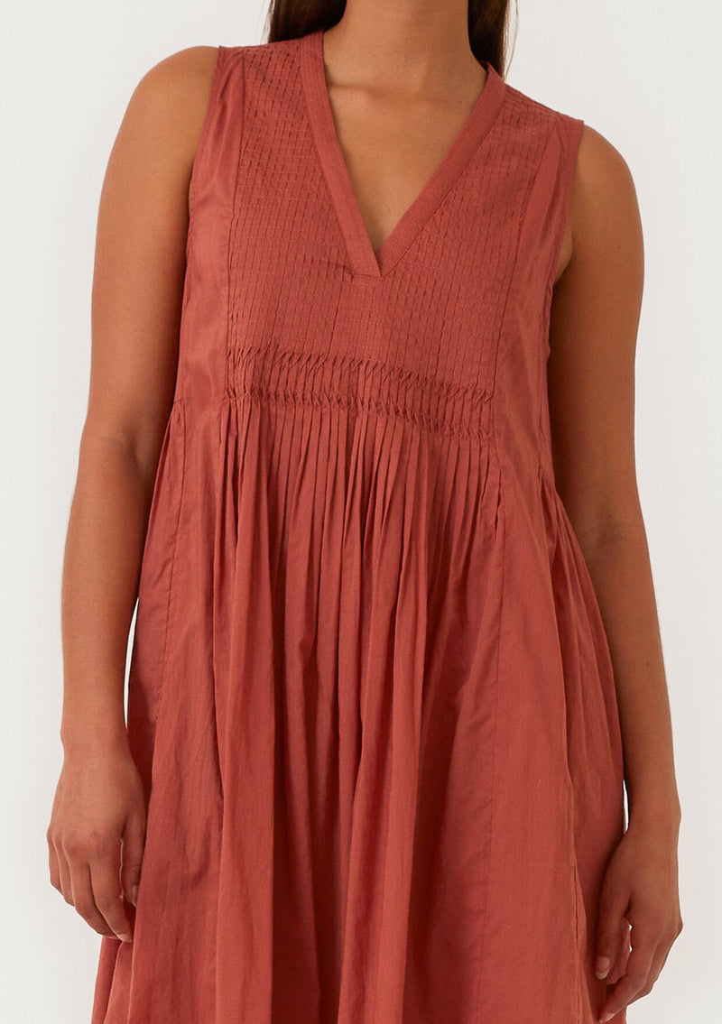 [Color: Rust] A close up front facing image of a brunette model wearing a lightweight bohemian sleeveless maxi tent dress in rust red. With a v neckline, pleated details, and side pockets. 