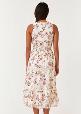 [Color: Natural/Dusty Wine] A back facing image of a brunette model wearing a sleeveless bohemian mid length dress in an off white and pink floral print. With a ruffle trimmed scoop neckline, a self covered button front top, a tiered skirt, lace trim, pintuck details, and a drawstring waist with ties. 