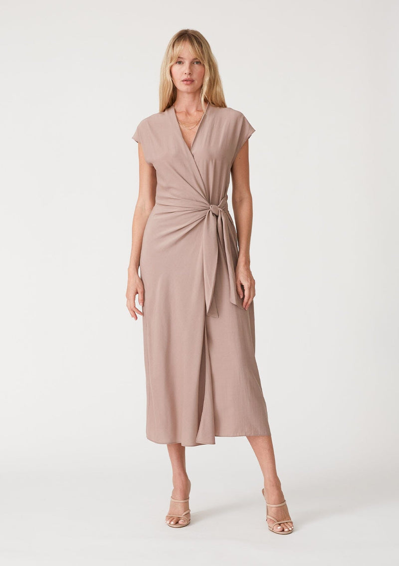 [Color: Mocha] A front facing image of a blonde model wearing a light brown maxi length wrap dress. With short cap sleeves, a deep v neckline, and a side tie waist closure. 