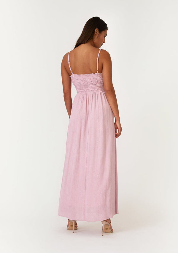 [Color: Orchid] A back facing image of a brunette model wearing an orchid purple sleeveless maxi dress with gold metallic thread details. With a ruffle trimmed straight neckline, an elastic waist, adjustable spaghetti straps, and a long flowy skirt. 