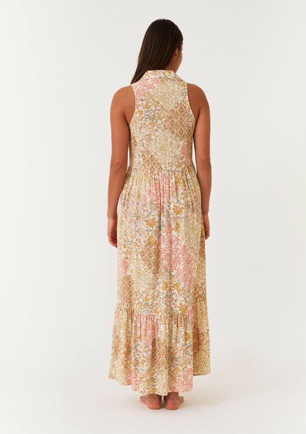 [Color: Dusty Peach/Rust] A back facing image of a brunette model wearing a bohemian sleeveless maxi dress designed in a peach and rust floral print. With a collared neckline, a self covered button front top, a long tiered skirt, and side pockets. 