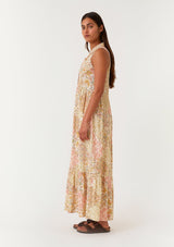 [Color: Dusty Peach/Rust] A side facing image of a brunette model wearing a bohemian sleeveless maxi dress designed in a peach and rust floral print. With a collared neckline, a self covered button front top, a long tiered skirt, and side pockets. 