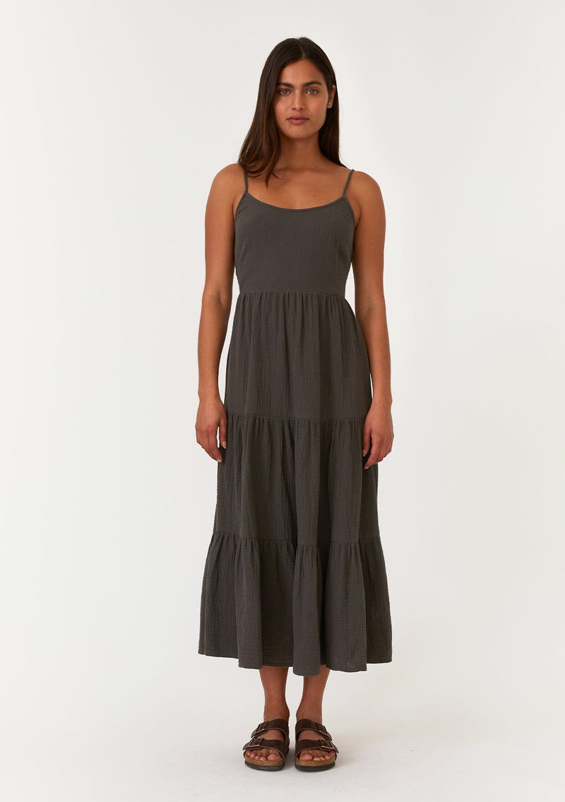 [Color: Lagoon] A full body front facing image of a brunette model wearing a sleeveless army green mid length spring dress. With adjustable spaghetti straps, a scoop neckline, a tiered skirt, and a half smocked elastic bodice at the back. 