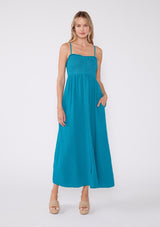 [Color: Teal Blue] A teal blue bohemian maxi dress made with soft cotton gauze. With adjustable spaghetti straps, a smocked bodice, a long flowy skirt, a self covered button front, side pockets, an empire waist, and a straight neckline with ruffle trim.