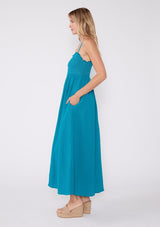 [Color: Teal Blue] A teal blue bohemian maxi dress made with soft cotton gauze. With adjustable spaghetti straps, a smocked bodice, a long flowy skirt, a self covered button front, side pockets, an empire waist, and a straight neckline with ruffle trim.