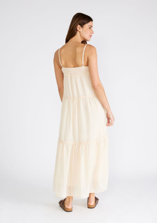 [Color: Light Peach] A back facing image of a brunette model wearing a light peach pink sleeveless maxi dress. A lightweight bohemian style with embroidered detail at the neckline, adjustable spaghetti straps, a lace trimmed tiered skirt, a straight neckline, and a long flowy fit. 