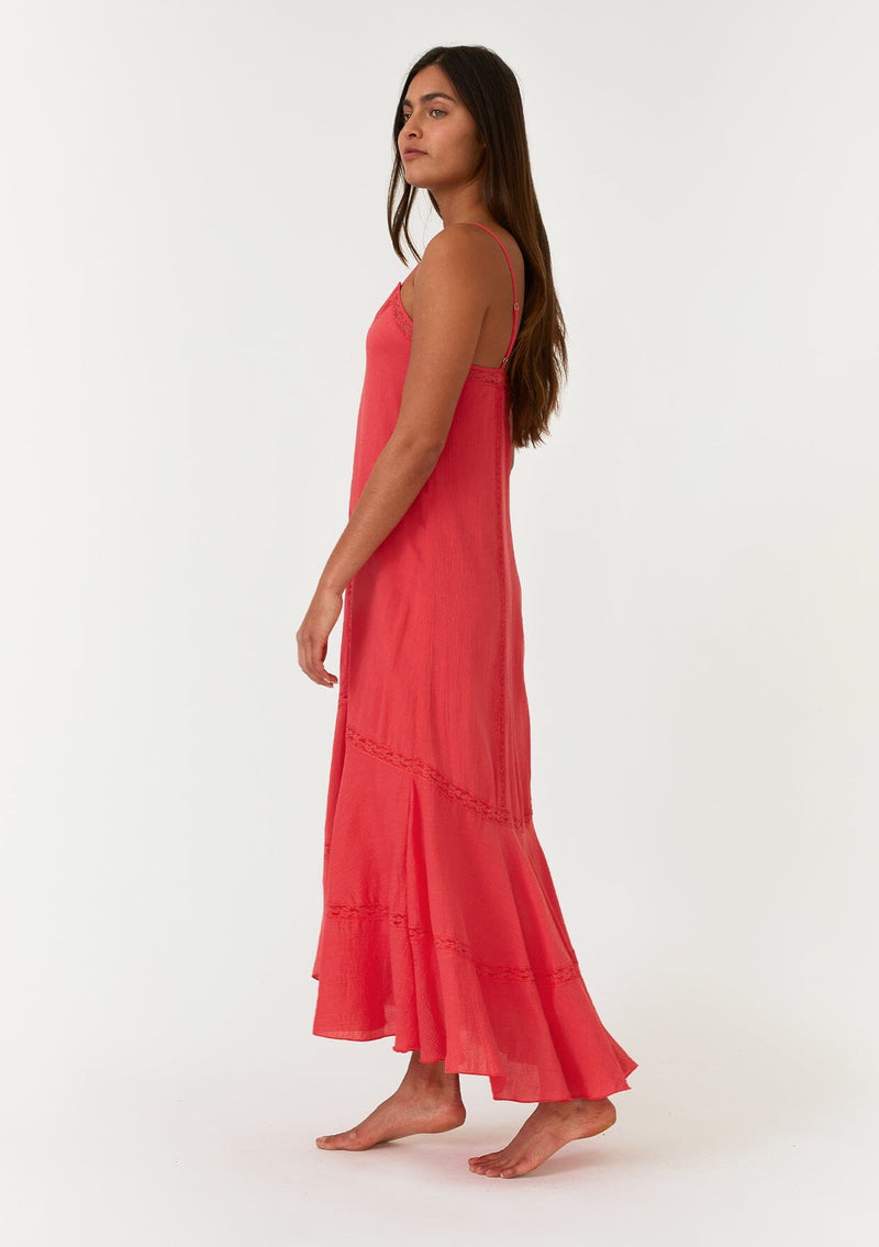 [Color: Hibiscus] A side facing image of a bright red bohemian sleeveless maxi dress. With adjustable spaghetti straps, a v neckline, a flowy tiered skirt with a high low hemline, a loop button up back detail, and lace trim. 