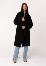 [Color: Black] A full body front facing image of a brunette model wearing a best selling oversized black cardigan. A cozy and thick sweater coat with a hood, an open front, side pockets, a cocoon style silhouette, and a mid length hem. 