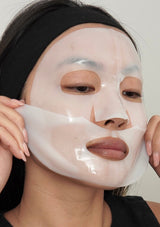 Person applying a white face mask to their face against a neutral background