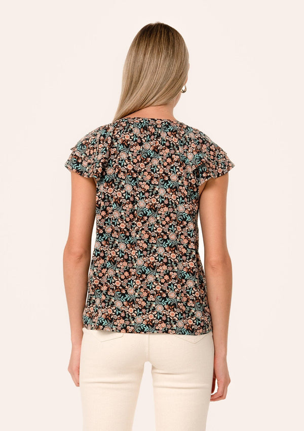 [Color: Black/Teal] A back facing image of a blonde model wearing a bohemian fall blouse in a black and teal floral print. With a self covered button front, double flutter short cap sleeves, and neck ties. 