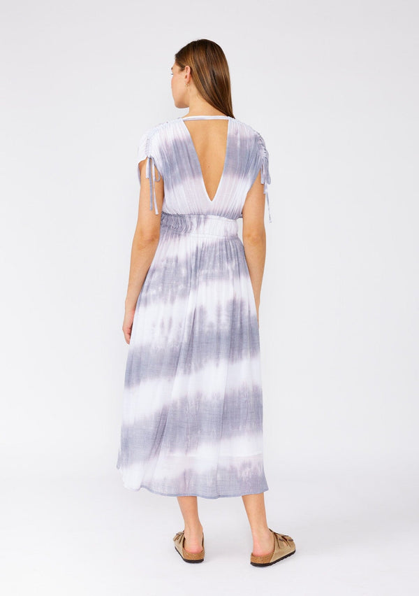 [Color: Off White/Grey] A back facing image of a brunette model wearing a bohemian mid length spring dress in a white and grey stripe. With short dolman sleeves, adjustable ties at the shoulder, an elastic waist, and a double v neckline in the front and back. 