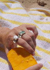 Hand with multiple rings holding a piece of fruit on a striped towel
