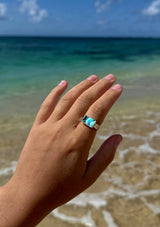 Hand wearing a ring with a blue gemstone by the ocean
