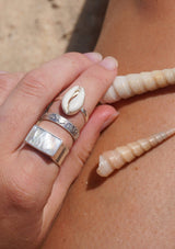 Hand wearing silver rings with shell designs on a sandy background