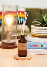 An amber glass diffuser bottle with a kraft label and rattan reeds. The Gold Coast Diffuser from PF Candle.