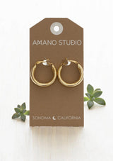 Gold hoop earrings on a 'Amano Studio' branded card with succulents in the background.