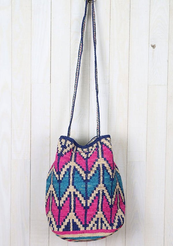[Color: Hot Pink/Turquoise] A bohemian bucket bag with pink and blue chevron stripe details, made from raffia. With a thick shoulder strap, a drawstring closure, and oversized tassel details. 