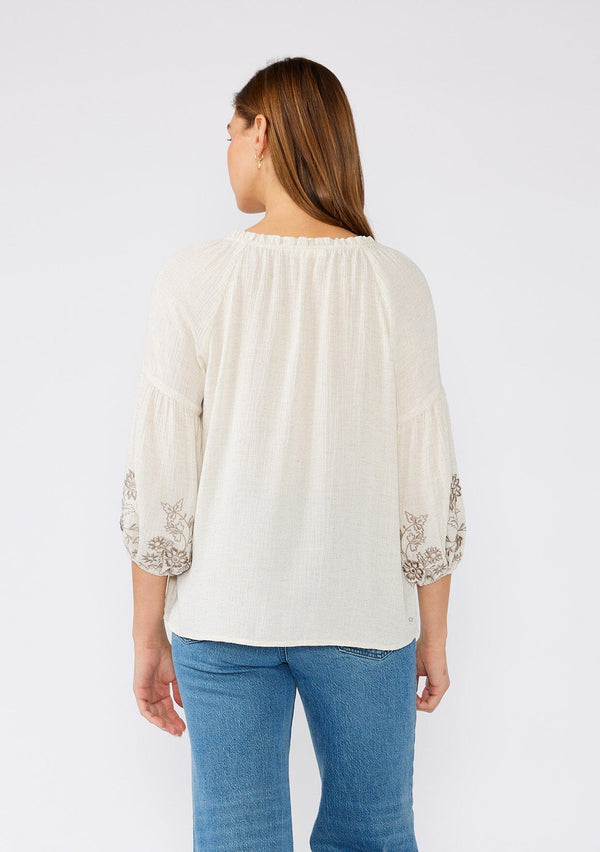 [Color: Natural/Taupe] A back facing image of a brunette model wearing an ivory flowy bohemian peasant top with embroidered detail and tassel ties.