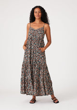 [Color: Black/Teal] A front facing image of a brunette model wearing a bohemian maxi dress in a black and teal floral print. With adjustable spaghetti straps, a scalloped trim v neckline with contrast thread details, a tiered flowy silhouette, side pockets, and an empire waist.