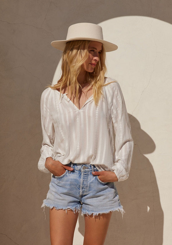 [Color: White] A front facing image of a blonde model standing outside wearing a bohemian white blouse with embroidered details. With long raglan sleeves, a round neckline with a single button closure, a front keyhole, and a relaxed fit.