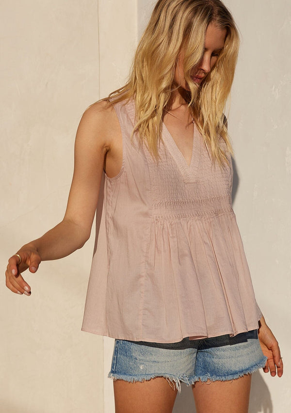 [Color: Mauve] A front facing image of a blonde model standing outside wearing a bohemian cotton tank top in a light mauve purple. With a v neckline, a loose, tent silhouette, and pleated details along the front. 
