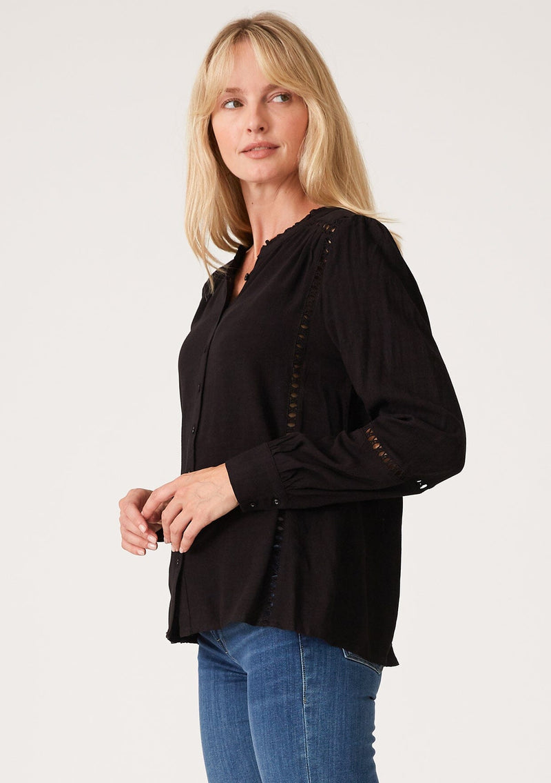 [Color: Black] A side facing image of a blonde model wearing a black linen blend bohemian blouse. With voluminous long sleeves, delicate crochet trim, and a self covered button front.