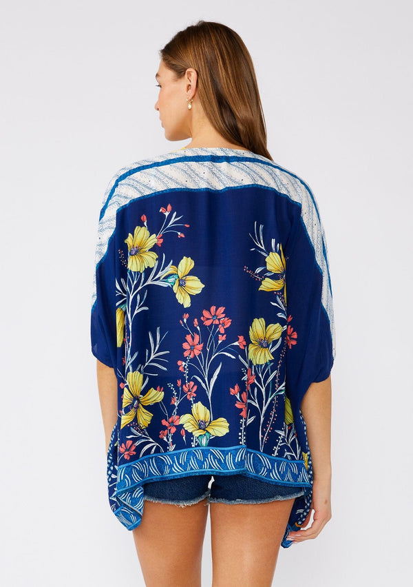 [Color: Navy/Yellow] A back facing image of a brunette model wearing a bohemian style kimono top in a navy blue and yellow floral print with a contrast border. A lightweight beach cover up style with half length sleeves, an open front, and a hip length hemline. 