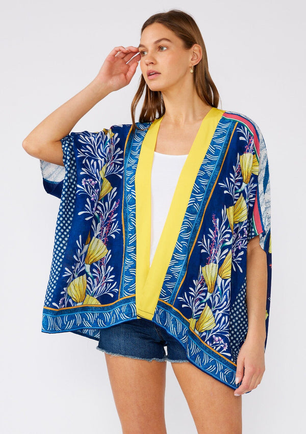 [Color: Navy/Yellow] A front facing image of a brunette model wearing a bohemian style kimono top in a navy blue and yellow floral print with a contrast border. A lightweight beach cover up style with half length sleeves, an open front, and a hip length hemline. 