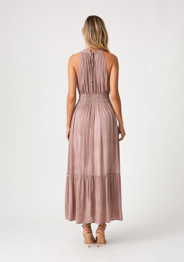 [Color: Rose Water] A back facing image of a blonde model wearing a pink bohemian maxi dress in a soft pink vintage wash. With a ruffle trimmed halter neckline, a smocked elastic waist, a tiered long skirt, and a back keyhole detail with an adjustable tie. 