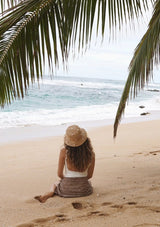 A blonde model wearing a raffia bucket hat with sewn in cowry shells.