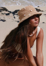 A blonde model wearing a raffia bucket hat with sewn in cowry shells.
