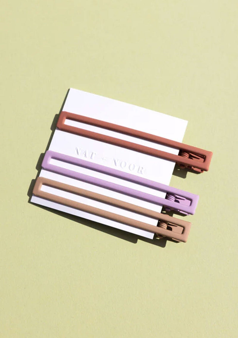 [Color: Sunset] A set of three long alligator style metal hair clips in coral, lavender, and nude.