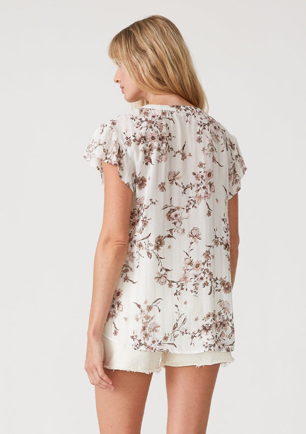 [Color: Ivory/Taupe] A back facing image of a blonde model wearing a lightweight spring top in a white and taupe purple floral print, with metallic thread detail. With short flutter sleeves, a relaxed fit, and a split v neckline. 