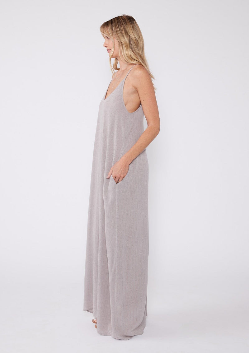 [Color: Lilac Dove] A side facing image of a blonde model wearing a light purple sleeveless maxi dress with gold metallic thread details. With adjustable spaghetti straps, a deep v neckline in the front and back, side pockets, and a loose, oversized flowy fit.