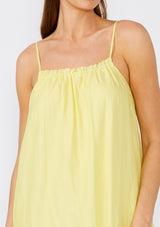 [Color: Lemon/Coral] A close up front facing image of a brunette model wearing a bohemian summer cotton maxi dress in a yellow tie dye print. With adjustable spaghetti straps, a scooped neckline with ruffled trim, a roomy fit, and side pockets. 