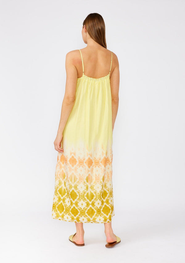 [Color: Lemon/Coral] A back facing image of a brunette model wearing a bohemian summer cotton maxi dress in a yellow tie dye print. With adjustable spaghetti straps, a scooped neckline with ruffled trim, a roomy fit, and side pockets. 