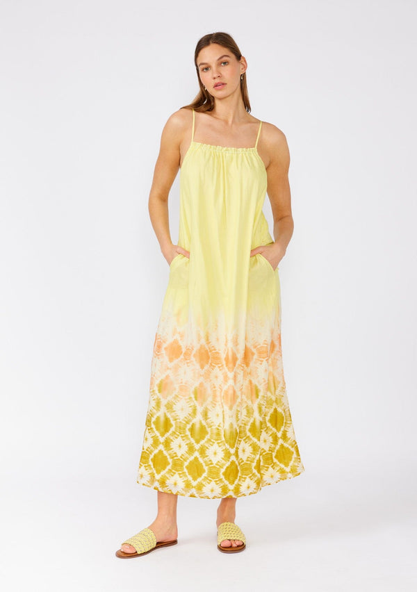 [Color: Lemon/Coral] A front facing image of a brunette model wearing a bohemian summer cotton maxi dress in a yellow tie dye print. With adjustable spaghetti straps, a scooped neckline with ruffled trim, a roomy fit, and side pockets. 