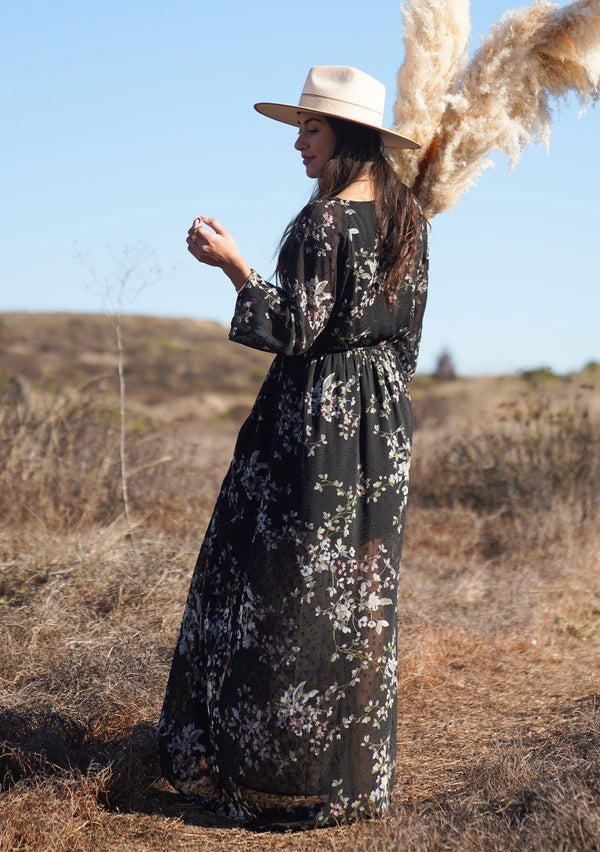 [Color: Black Slate] The ultimate romantic Autumn dress is here. Our bohemian floral print maxi dress is designed in a delicate sheer clip dot. Featuring a self covered button up front, a cinched elastic waist for definition, and voluminous long sleeves with a smocked elastic wrist cuff. A gorgeous day to night maxi dress. 