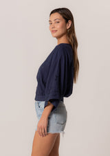 [Color: Navy] A side facing image of a brunette model wearing a bohemian navy blue embroidered eyelet top with billowy half length sleeves, a button front, and a v neckline.