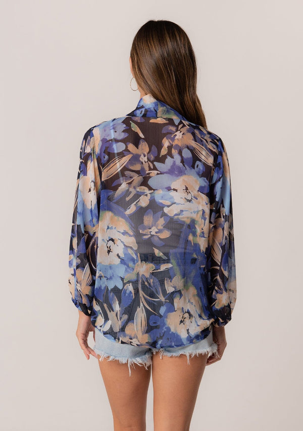 [Color: Navy/Light Blue] A back facing image of a brunette model wearing a sheer chiffon tie front top in a blue floral print. With long sleeves, a deep v neckline, a flowy relaxed fit, and a tie front waist detail. 