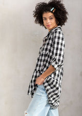 [Color: Black/White] A model wearing a relaxed cotton blend black large gingham button up tunic, with a rolled sleeve, a tiered body, and a long tunic length.